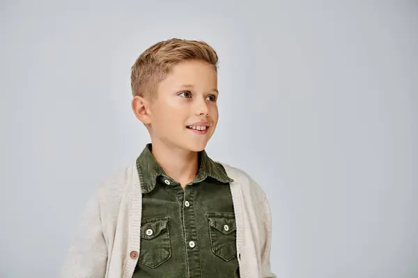 Gioioso bambino in caldo cardigan casual sorridente e guardando lontano su sfondo grigio, concetto di moda — Foto stock