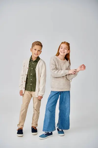 Cheerful preadolescent children in stylish casual clothes posing on gray backdrop, smiling at camera — Stock Photo