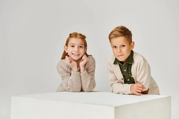 Happy preteen children posing next to white cube and smiling at camera, hands under chin, fashion — Stock Photo
