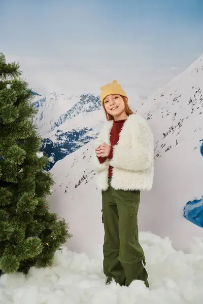 Colpo verticale di preadolescente allegra ragazza in inverno elegante abbigliamento sorridente alla macchina fotografica in piedi sulla neve — Foto stock