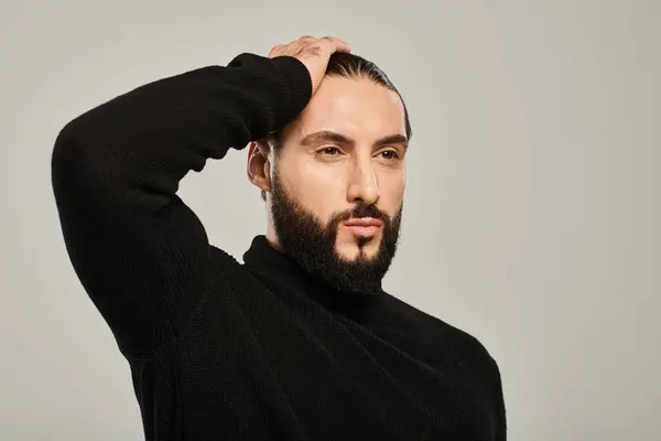 Retrato de hombre árabe guapo con barba posando en cuello alto negro sobre fondo gris - foto de stock