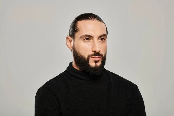 Portrait of good looking arabic man with beard posing in black turtleneck on grey background — Stock Photo