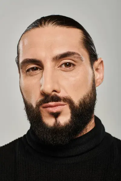 Retrato de homem árabe masculino com barba posando em gola alta preta sobre fundo cinza — Fotografia de Stock