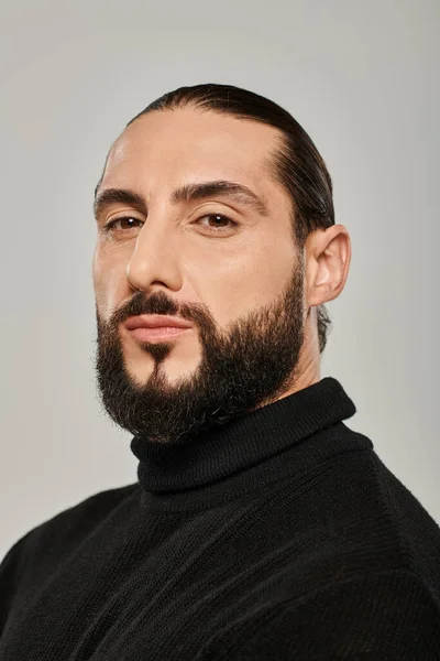 Retrato de hombre árabe masculino con barba posando en cuello alto negro sobre fondo gris - foto de stock