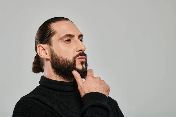 Portrait of good looking arabic man in turtleneck touching beard and posing on grey backdrop — Stock Photo