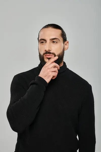 Portrait of handsome arabic man in turtleneck touching beard while thinking on grey backdrop — Stock Photo