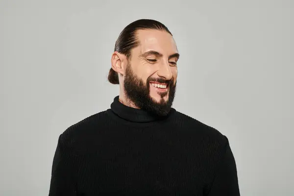 Portrait of good looking arabic man with beard posing in turtleneck and smiling on grey backdrop — Stock Photo