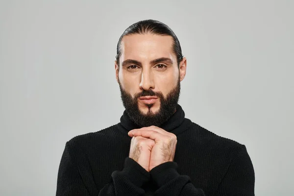 Portrait d'un homme arabe barbu frappant au col roulé noir regardant la caméra sur fond gris — Photo de stock