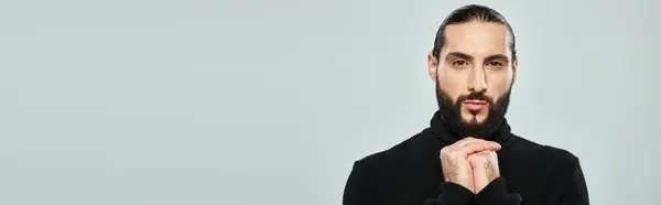 Portrait of bearded arabic man in black turtleneck looking at camera on grey backdrop, banner — Stock Photo