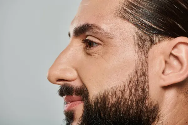 Perfil de hombre árabe alegre con barba sonriente y mirando hacia otro lado sobre fondo gris - foto de stock