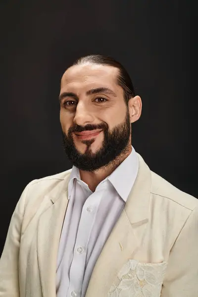 Hombre árabe feliz y barbudo en camisa blanca y chaqueta mirando a la cámara sobre fondo negro - foto de stock