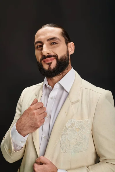 Happy and bearded arabic man in white shirt and blazer looking at camera on black background — Stock Photo