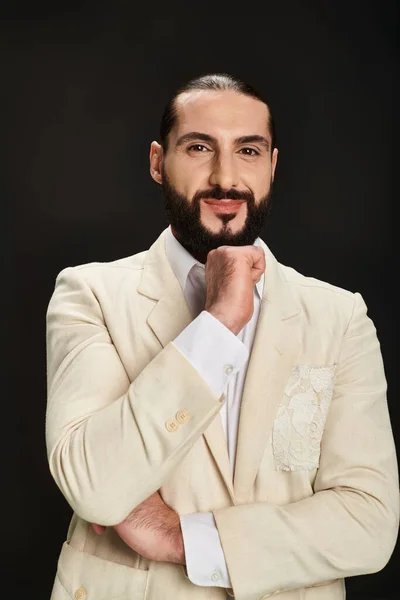 Hombre árabe barbudo alegre en camisa blanca y chaqueta mirando a la cámara sobre fondo negro - foto de stock