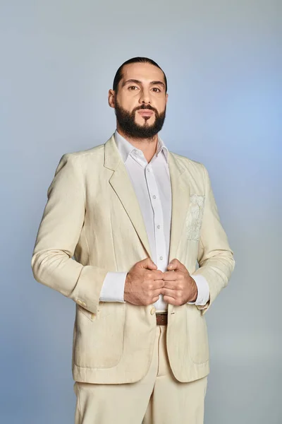 Hombre de moda y barbudo en camisa blanca y chaqueta posando sobre fondo gris, elegante atuendo - foto de stock