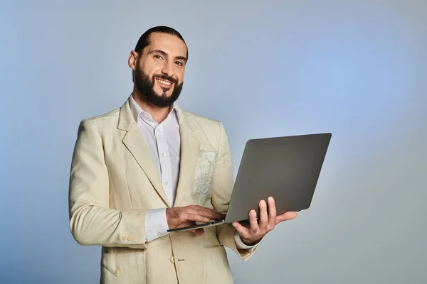 Bearded arabic man in elegant formal wear using laptop on grey background, digital age — Stock Photo