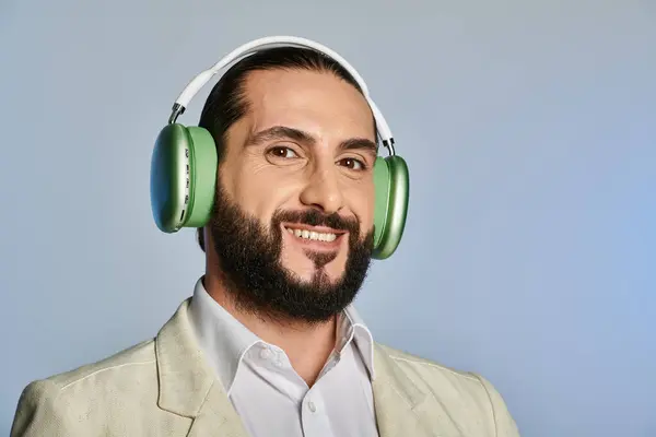 Glücklicher bärtiger Mann in eleganter formaler Kleidung, der Musik in drahtlosen Kopfhörern auf grauem Hintergrund hört — Stockfoto