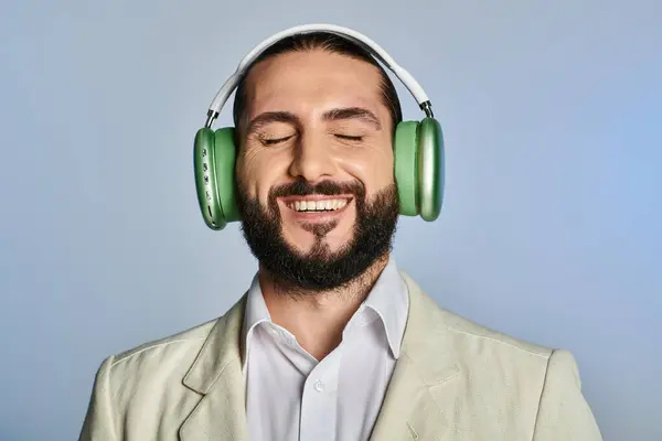 Happy bearded man in elegant formal wear listening music in wireless headphones on grey, closed eyes — Stock Photo