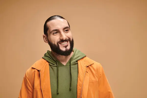 Porträt eines fröhlichen und bärtigen arabischen Mannes in legerer Kleidung, der auf beigem Hintergrund lächelt — Stockfoto