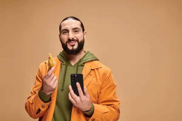 Happy man holding baklava and using smartphone on beige backdrop, traditional middle eastern dessert — Stock Photo