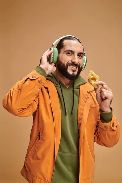 Happy arabic man in headphones holding honey baklava on beige background, middle eastern dessert — Stock Photo