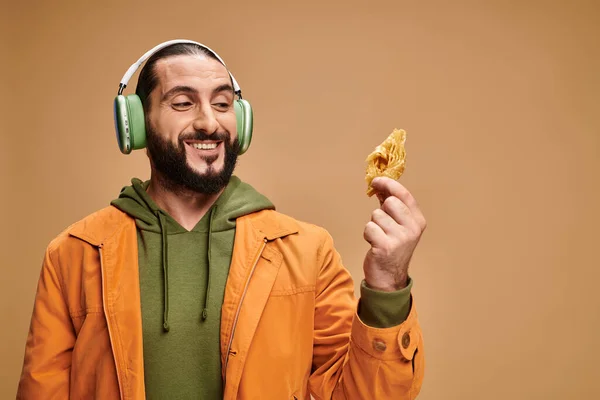 Happy arabic man in headphones holding honey baklava on beige background, middle eastern dessert — Stock Photo