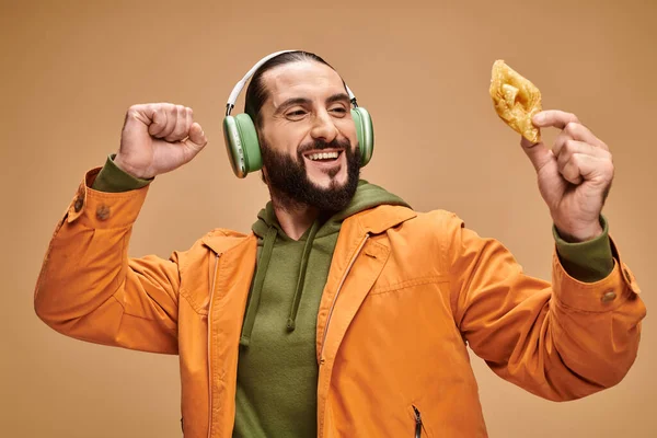 Glücklicher arabischer Mann mit Kopfhörern, der Honig-Baklava auf beigem Hintergrund hält, nahöstliches Dessert — Stockfoto