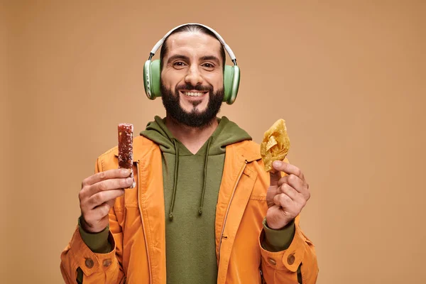 Happy arabic man in headphones holding two middle eastern desserts, honey baklava and churchkhela — Stock Photo