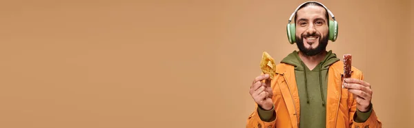 Homme heureux dans les écouteurs tenant deux desserts du Moyen-Orient, baklava miel et bannière churchkhela — Photo de stock