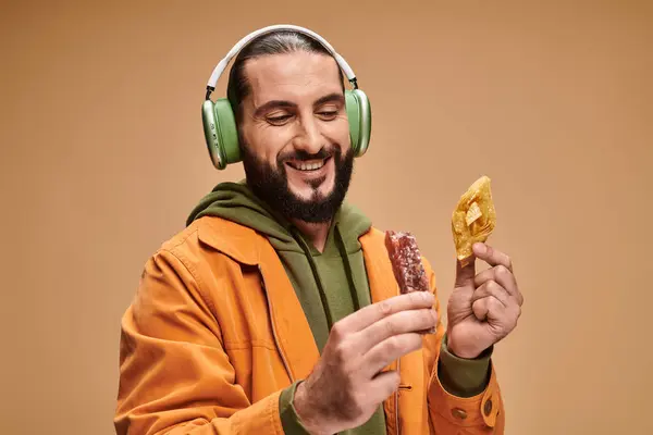 Homme heureux dans les écouteurs tenant deux desserts du Moyen-Orient, miel baklava et churchkhela — Photo de stock