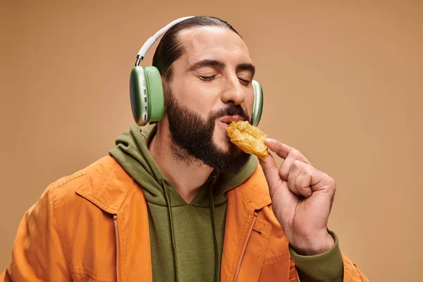 Happy man in headphones eating delicious honey baklava on beige backdrop, turkish delights — Stock Photo