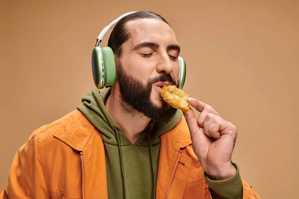 Homme heureux dans les écouteurs manger délicieux miel baklava sur fond beige, plaisirs turcs — Photo de stock