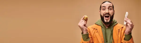 Excité homme barbu tenant baklava et cevizli sucuk sur fond beige, turque délices bannière — Photo de stock