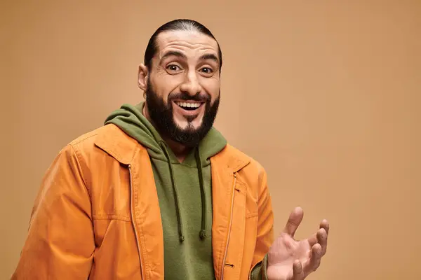Fröhlicher arabischer Mann mit Bart, der lässig gekleidet vor beigem Hintergrund in die Kamera blickt — Stockfoto
