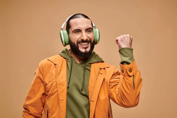 Alegre homem do Oriente Médio com barba ouvindo música em fones de ouvido sem fio no fundo bege — Fotografia de Stock