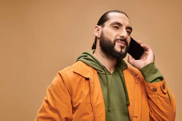 Красивый ближневосточный мужчина с бородой разговаривает на смартфоне на бежевом фоне, цифровой век — стоковое фото
