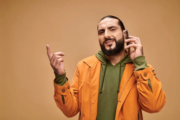Emotional middle eastern man with beard talking on smartphone on beige background, banner — Stock Photo