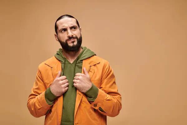 Pensativo hombre de Oriente Medio con barba de pie en traje casual sobre fondo beige, mirando hacia otro lado - foto de stock