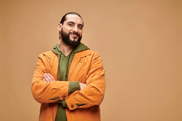 Pleased middle eastern man with beard standing in casual attire with crossed arms on beige backdrop — Stock Photo