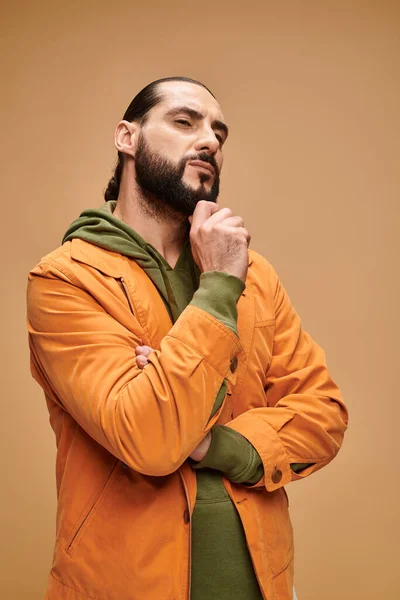 Nachdenklicher Mann aus dem Mittleren Osten mit Bart steht in lässiger Kleidung vor beigem Hintergrund und schaut weg — Stockfoto