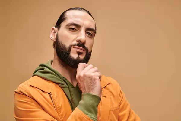 Nachdenklicher Mann aus dem Mittleren Osten streift Bart und steht in legerer Kleidung auf beigem Hintergrund — Stockfoto