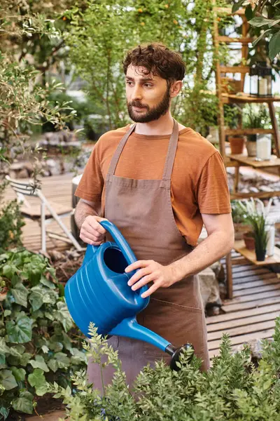 Jardineiro profissional em avental de linho regar arbusto verde com regador azul em estufa — Fotografia de Stock