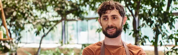 Professional headshots, cheerful bearded gardener in apron and gloves posing in greenhouse, banner — Stock Photo
