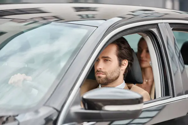 Confident bearded man driving luxury car with businesswoman on rear seat on blurred background — Stock Photo
