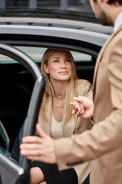 Розмитий чоловік тримає руку усміхненої блондинки-бізнесу в офіційному одязі, витягуючи розкішний автомобіль — стокове фото