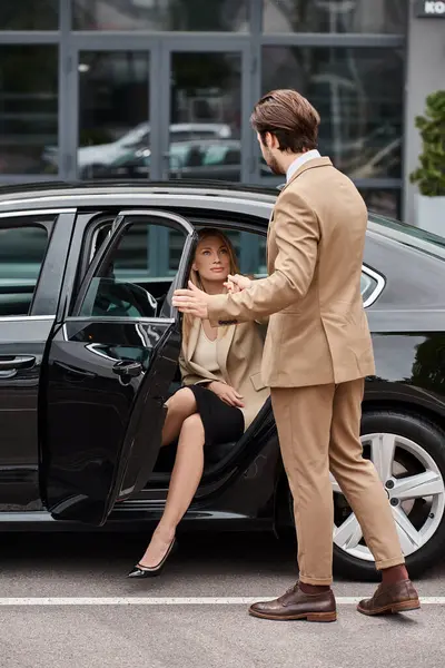 Élégant homme tenant la main de blonde femme d'affaires en tenue de cérémonie sortir voiture de luxe sur la rue — Photo de stock
