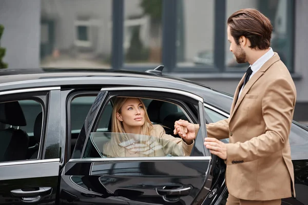 Homme en tenue formelle tenant la main d'élégante femme d'affaires blonde sortir voiture de luxe sur la rue — Photo de stock