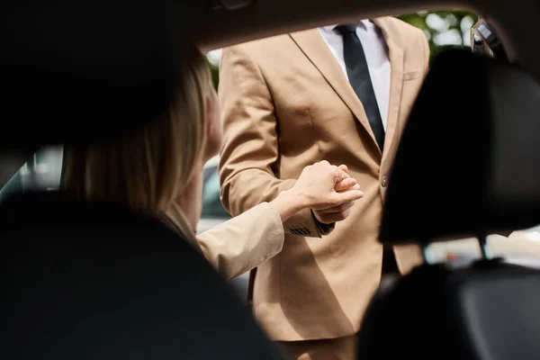 Обрезанный вид стильного мужчины, держащего за руку элегантную женщину в формальной одежде, выходящую из машины на улицу — стоковое фото
