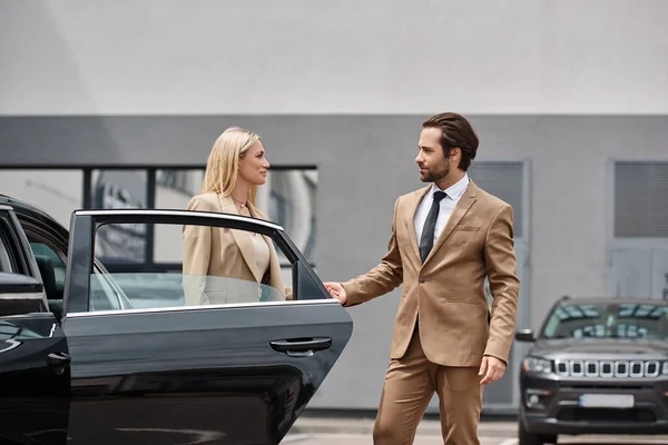 Bearded elegant man and stylish blonde businesswoman holding hands near luxury car on city street — Stock Photo
