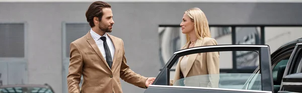 Bearded stylish man and elegant blonde businesswoman holding hands near luxury car on street, banner — Stock Photo