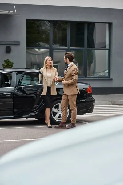 Elegante pareja de negocios en formal desgaste de la mano y mirando unos a otros cerca de coche en la calle - foto de stock